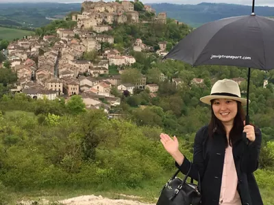 Accueil client avec parapluie devant un village, service VIP et transport privé personnalisé