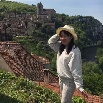 Voyageuse souriante avec chapeau devant un village et une vallée, excursion avec chauffeur privé